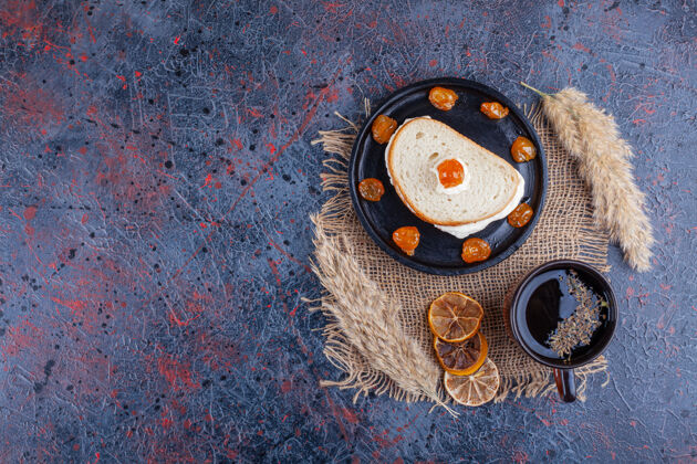 美味煎鸡蛋在两片面包之间放在一块木板上 旁边放一杯茶 背景是蓝色的面粉板美味