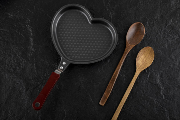 菜黑色表面的心形锅和木勺木头心锅