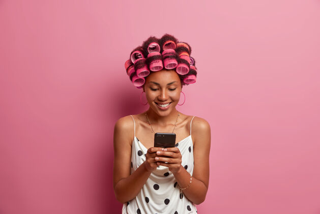 粉色积极的黑皮肤女人适用于完美的发型辊头发持有现代手机女士请手机