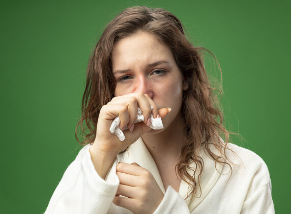 青咳嗽的年轻生病的女孩穿着白色长袍直直地向前看 手放在嘴上 隔离在绿色上穿口病