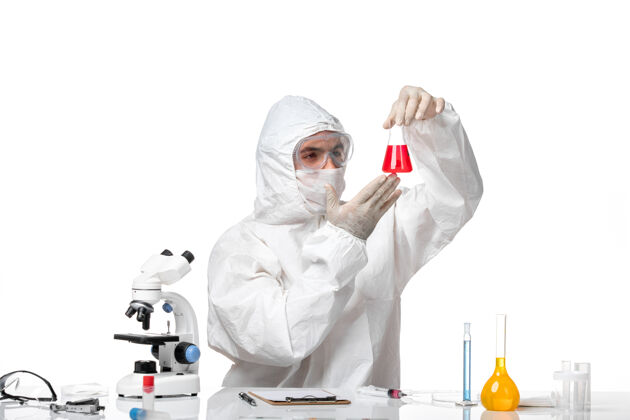 化学正面图：男医生穿着防护服 戴着口罩 白色桌子上放着一个装有红色溶液的瓶子视图人溶液