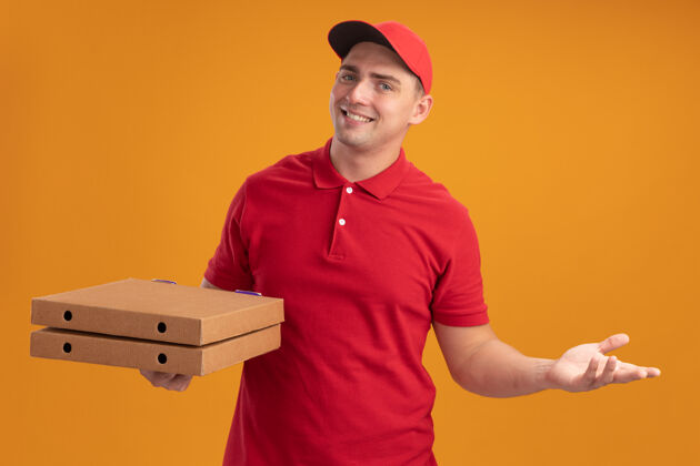制服微笑的年轻送货员身穿制服 头戴鸭舌帽 手里拿着披萨盒 手被隔离在橙色的墙上手摊开拿着