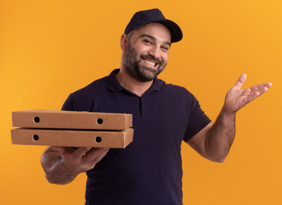 男人微笑着的中年送货员 穿着制服 戴着帽子 手里拿着披萨盒 手被隔离在黄色的墙上中年人微笑盒子