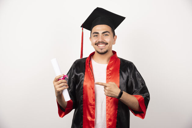 立场快乐的学生指着白色的文凭毕业帽子证书