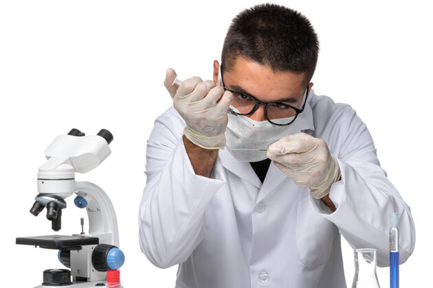 专业正面图男性医生穿着白色医疗服 戴着面罩 因为科维德在一个白色的空间里用溶液工作实验室外套观点男性医生