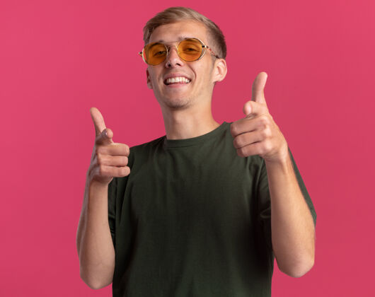 男人面带微笑的年轻帅哥 穿着绿色衬衫 戴着眼镜 在粉红色的墙上展示着你的姿势秀微笑戴