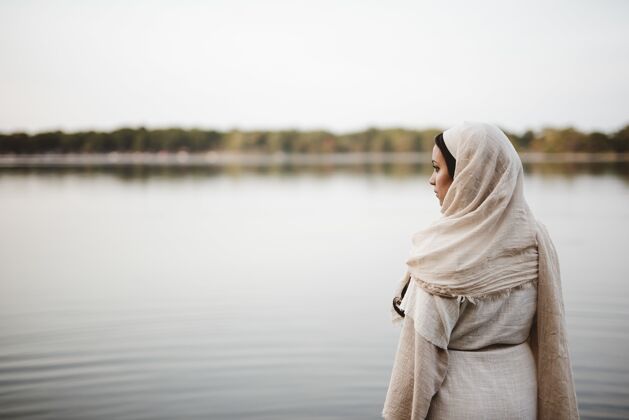 成人从一个穿着圣经长袍的女性的背后拍摄的浅焦点 同时看着远处服装年轻长袍