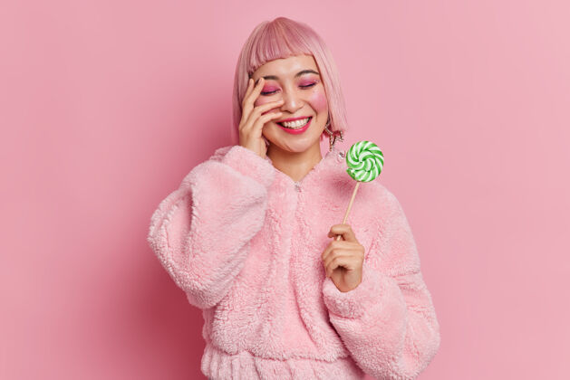 高兴积极的亚洲女人 粉色头发 明亮的妆容 手里拿着美味的糖果化妆品人姿势