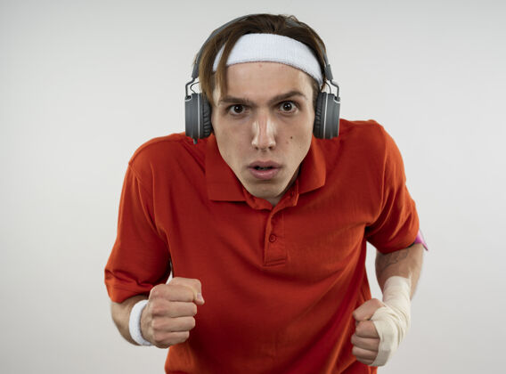 乐队自信的年轻人戴着带腕带的头带和带电话臂带的耳机 在白色的墙上显示出跑步的姿势耳机电话穿