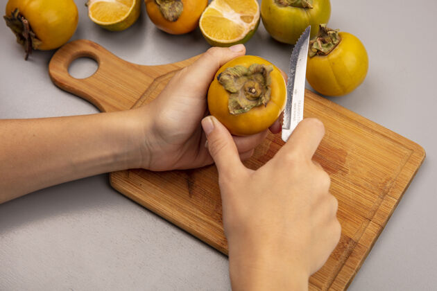 顶部女性手用刀在木制菜板上切新鲜柿子水果的俯视图板女水果