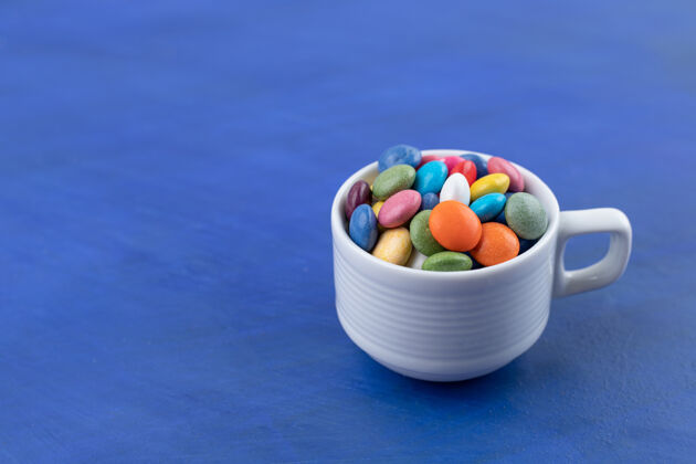 马克杯一个白色的杯子在蓝色的表面上装满了糖果美味含糖糖果