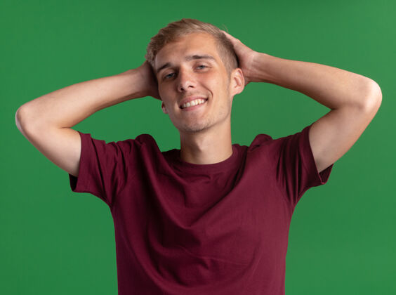 年轻微笑着的年轻帅哥穿着红衬衫把手放在脑后隔离在绿色的墙上手小伙子穿