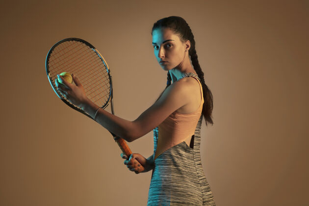 摄影棚射击一位白人女子在混合霓虹灯下孤立地打网球 背景是棕色适合年轻女性运动员在运动比赛中运动或动作运动 运动 健活方式的概念完整活动活动