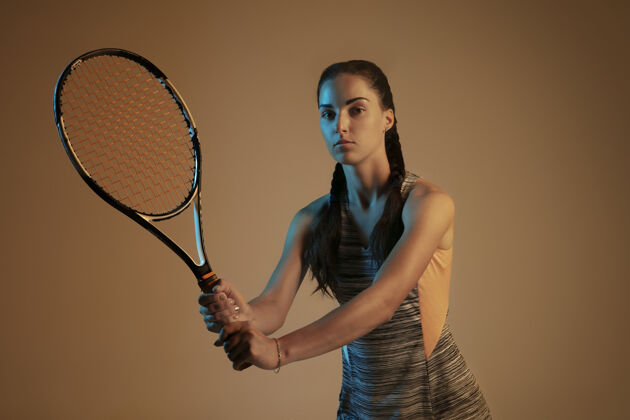 练习一位白人女子在混合霓虹灯下孤立地打网球 背景是棕色适合年轻女性运动员在运动比赛中运动或动作运动 运动 健活方式的概念女性完整跑步