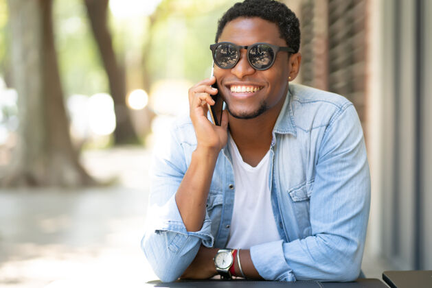 城市坐在咖啡店打电话的非裔美国人微笑电话科技