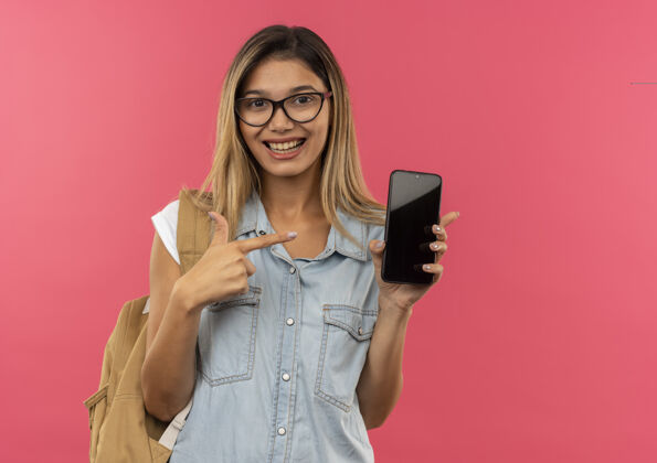 背快乐的年轻漂亮的女学生戴着眼镜 背着书包 拿着手机指着粉色的隔离带指着包粉色