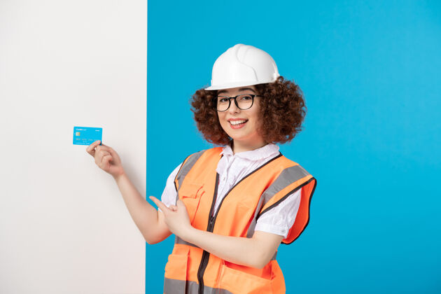 人前视图穿着制服的女建筑工人 蓝色信用卡在蓝色上信用漂亮女建筑工人
