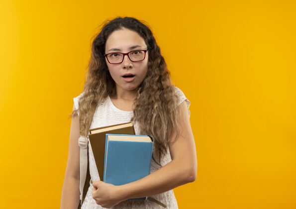 眼镜印象深刻的年轻漂亮的女学生戴着眼镜和背上的书包举行孤立的黄色包抱黄色