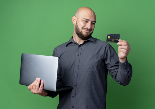 控股高兴的年轻秃头呼叫中心男子手持笔记本电脑和信用卡看着卡上的绿色背景隔离笔记本电脑信贷呼叫