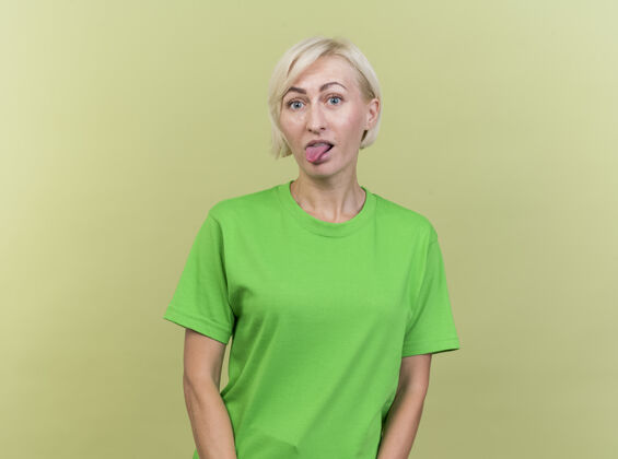摆姿势顽皮的中年金发斯拉夫女人看前面显示舌头孤立在橄榄绿的墙壁与复制空间斯拉夫人人感觉