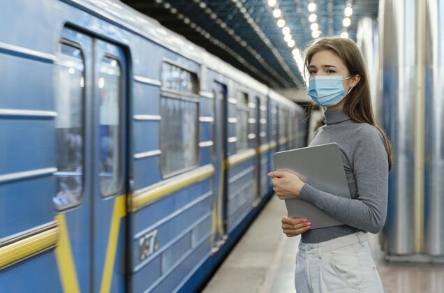 公共服务拿着平板电脑在地铁站等着的年轻女子旅行外科口罩地铁站