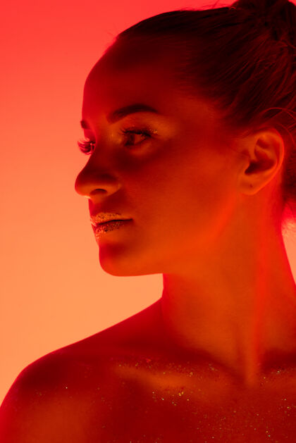 肖像在霓虹灯 单色 红橙色工作室背景上孤立的美女肖像美丽的女模特人类情感的概念 面部表情 销售 广告 时尚和美丽音乐家面部脸