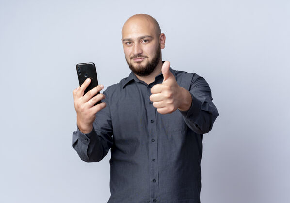 拇指高兴的年轻秃头呼叫中心男子手持手机 并显示拇指上孤立的白色背景与复制空间电话中间年轻