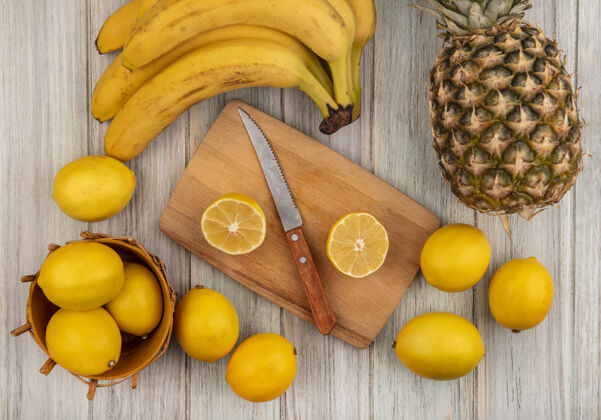 食品顶视图柑橘类水果柠檬放在桶上 半个柠檬放在木制厨房板上 刀子上有柠檬香蕉和菠萝 隔离在灰色木制背景上水果菠萝健康