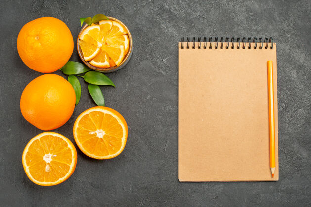 饮食一套黄色的完整的和切碎的橙子和笔记本放在深色的桌子上水果甜橙可食用水果