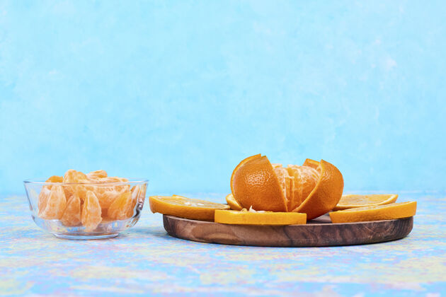 健康把橘子和柑桔切片 分别放在木制盘子和蓝色背景的玻璃杯中高质量的照片生物产品柑橘