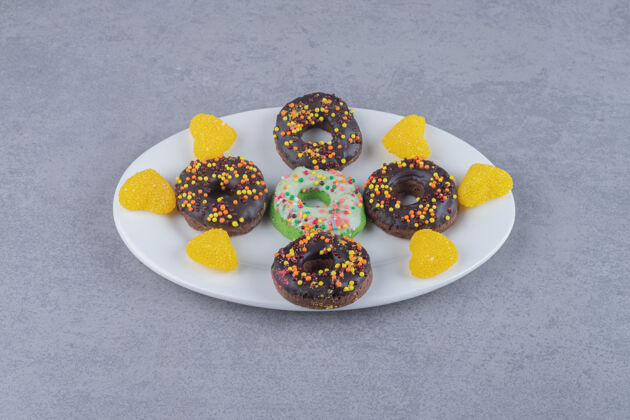 甜点小甜甜圈和marmelades整齐地排列在大理石表面的盘子上美味美味釉面