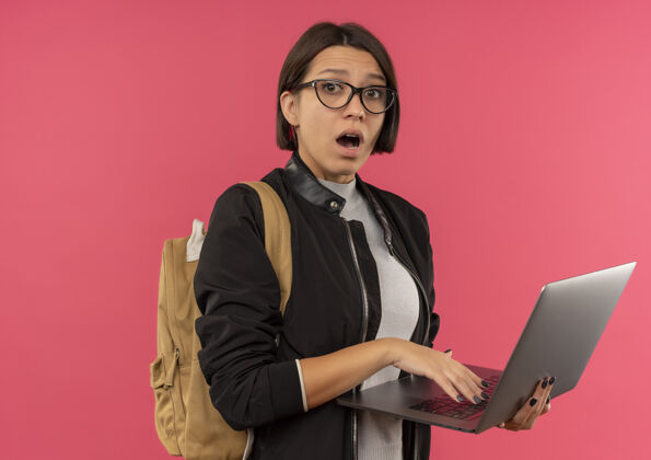 穿印象深刻的年轻女学生戴着眼镜 背着手提电脑的袋子上孤立的粉红色笔记本电脑学生眼镜