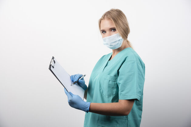 人女医生在剪贴板上写字 戴着医用口罩高质量的照片防护人女孩