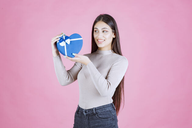 人拿着一个蓝色心形礼品盒的女孩在演示惊喜快乐休闲