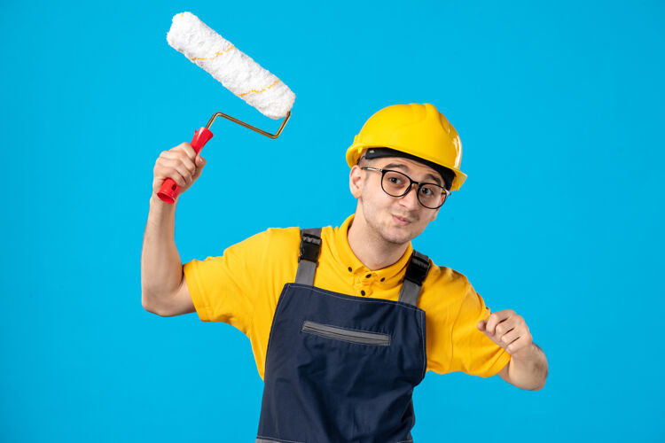手一个蓝色的表面上穿着制服 手里拿着油漆辊的男建筑工人的正视图制服前面工作