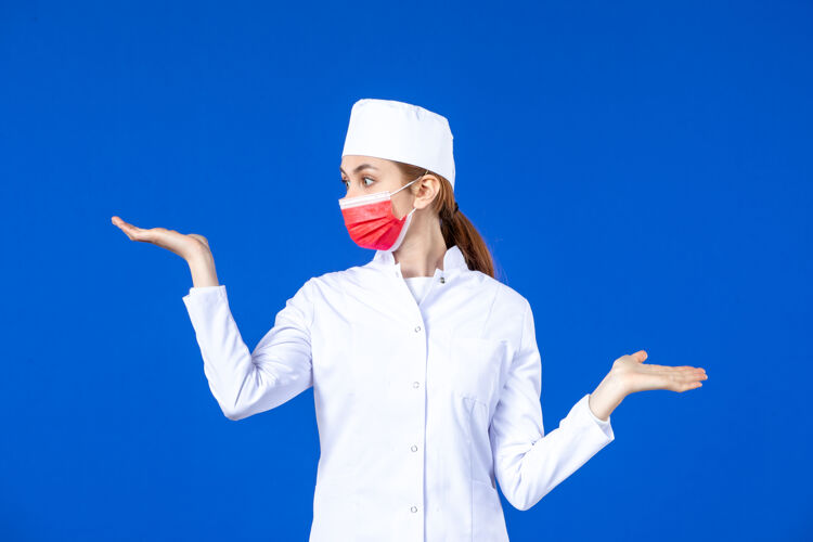 面具正面图身着医疗服的年轻护士 蓝色墙上戴着红色防护面具套装工作疾病