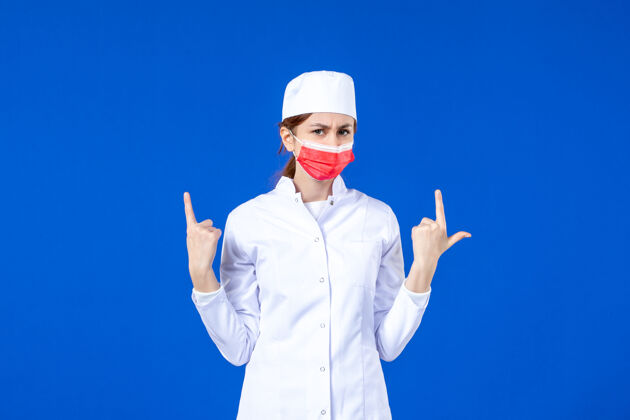 医院正面图身着医疗服的年轻护士 蓝色墙上戴着红色防护面具专业成人疾病