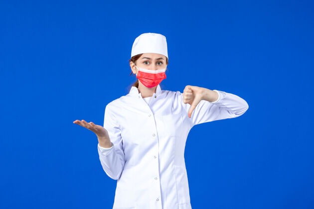 蓝色正面图身着医疗服的年轻护士 蓝色墙上戴着红色防护面具人员套装人员