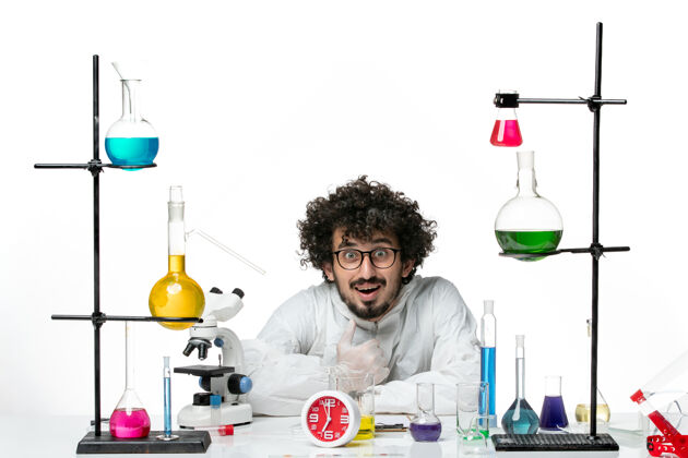 烧杯正面图穿着特殊套装的年轻男性科学家坐在浅白的墙上拿着解决方案化学溶液套装