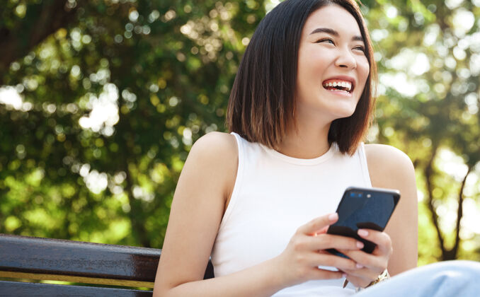 女孩快乐的亚洲女孩坐在长椅上用手机Wifi聊天亚洲
