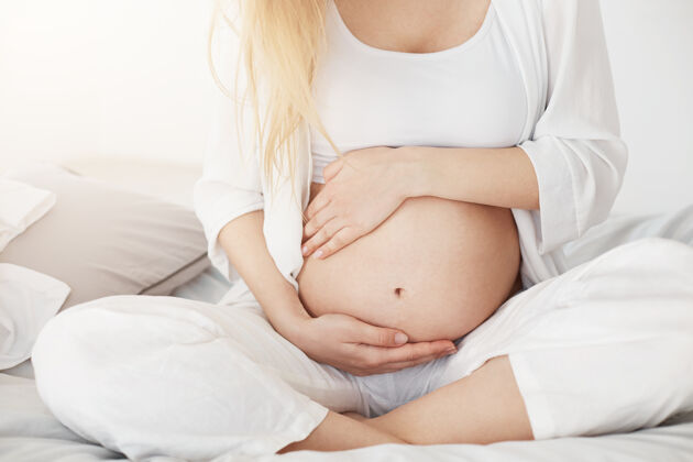 休闲怀孕不久的年轻准妈妈下午坐在卧室摸肚子怀孕概念年轻人人女人