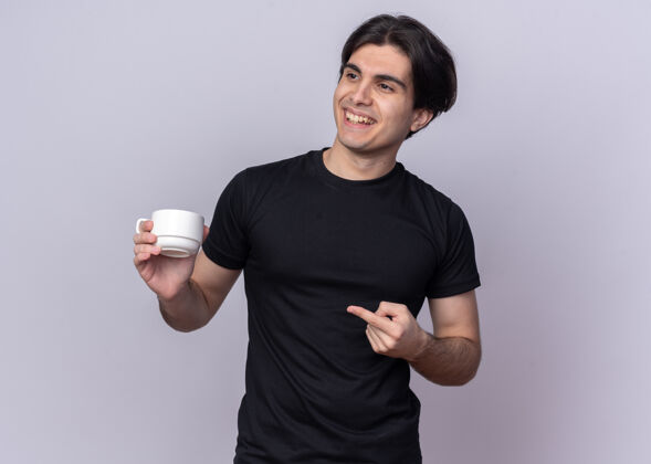 杯子面带微笑的年轻帅哥身穿黑色t恤 端着一杯咖啡点在一旁 隔离在白色的墙上 留有临摹空间点咖啡年轻