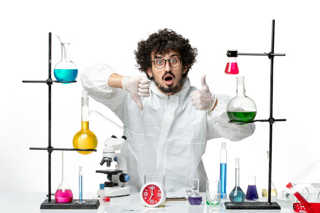 光正面图身着特殊套装的年轻男性科学家站在浅白的墙上 拿着解决方案围着桌子溶液实验室博士