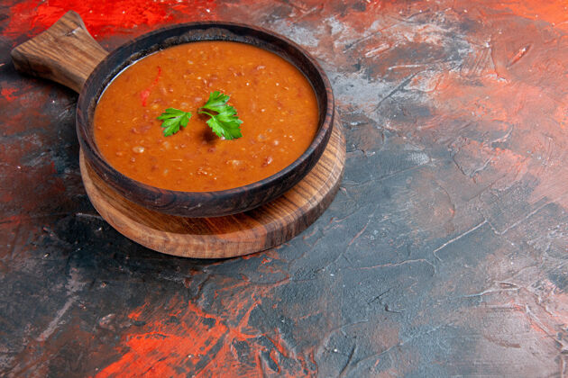 餐厅番茄汤的水平视图在一个棕色的砧板上 在一个混合颜色的桌子的右侧食物晚餐盘子