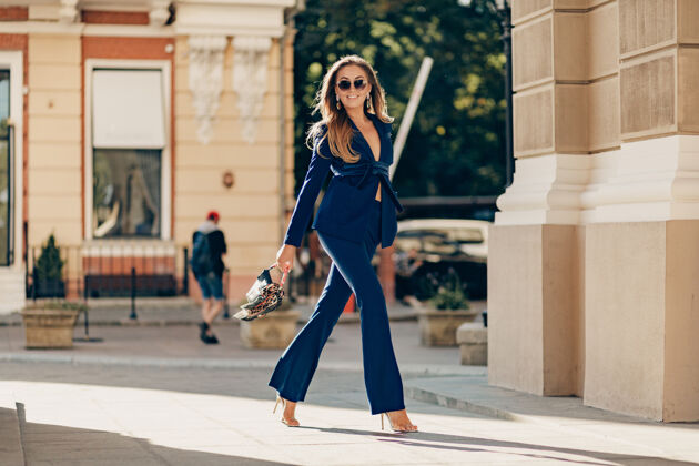 女人一位穿着优雅时尚的蓝色西装的奢华富婆 在阳光明媚的秋日手捧钱包漫步在城市人时尚衣服