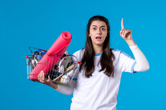 成人正面图年轻女子拿着装满运动用品的蓝墙篮子篮子前面视图