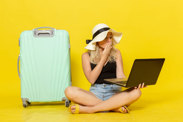 成人前视图年轻的女性使用她的笔记本电脑在黄墙上航行度假女性旅行太阳笔记本电脑视图肖像