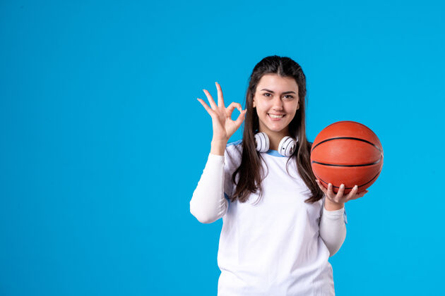篮球正面图：蓝色墙上挂着篮球的年轻女子成人比赛人