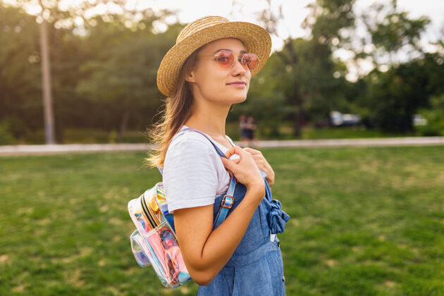 年轻戴着草帽 戴着粉色太阳镜 微笑着行走在公园里的年轻漂亮女人的肖像 夏日时尚的风格 五颜六色的时髦装扮阳光稻草魅力