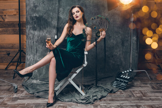女孩年轻时尚性感的女人坐在电影院后台的椅子上 用一杯香槟庆祝闪亮名人年轻